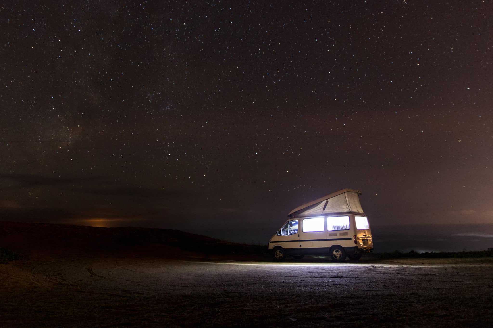 A camper van parked on a dirt road under a starry sky, available for RV Inspections.