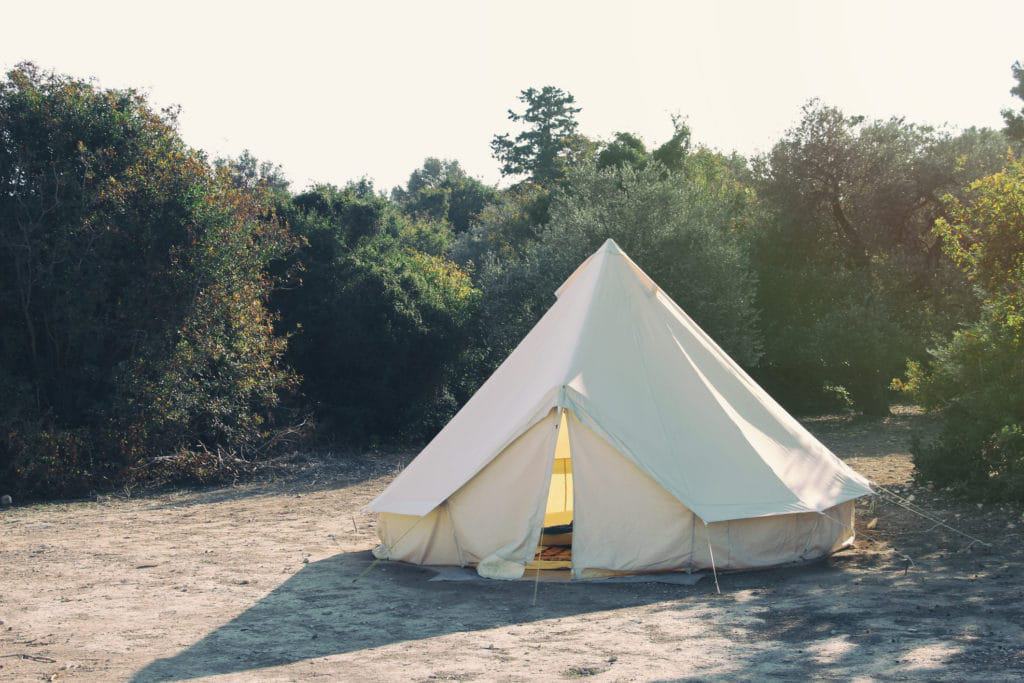 A UK glamping site offering poor service and overbooking with a white tent nestled in the woods.