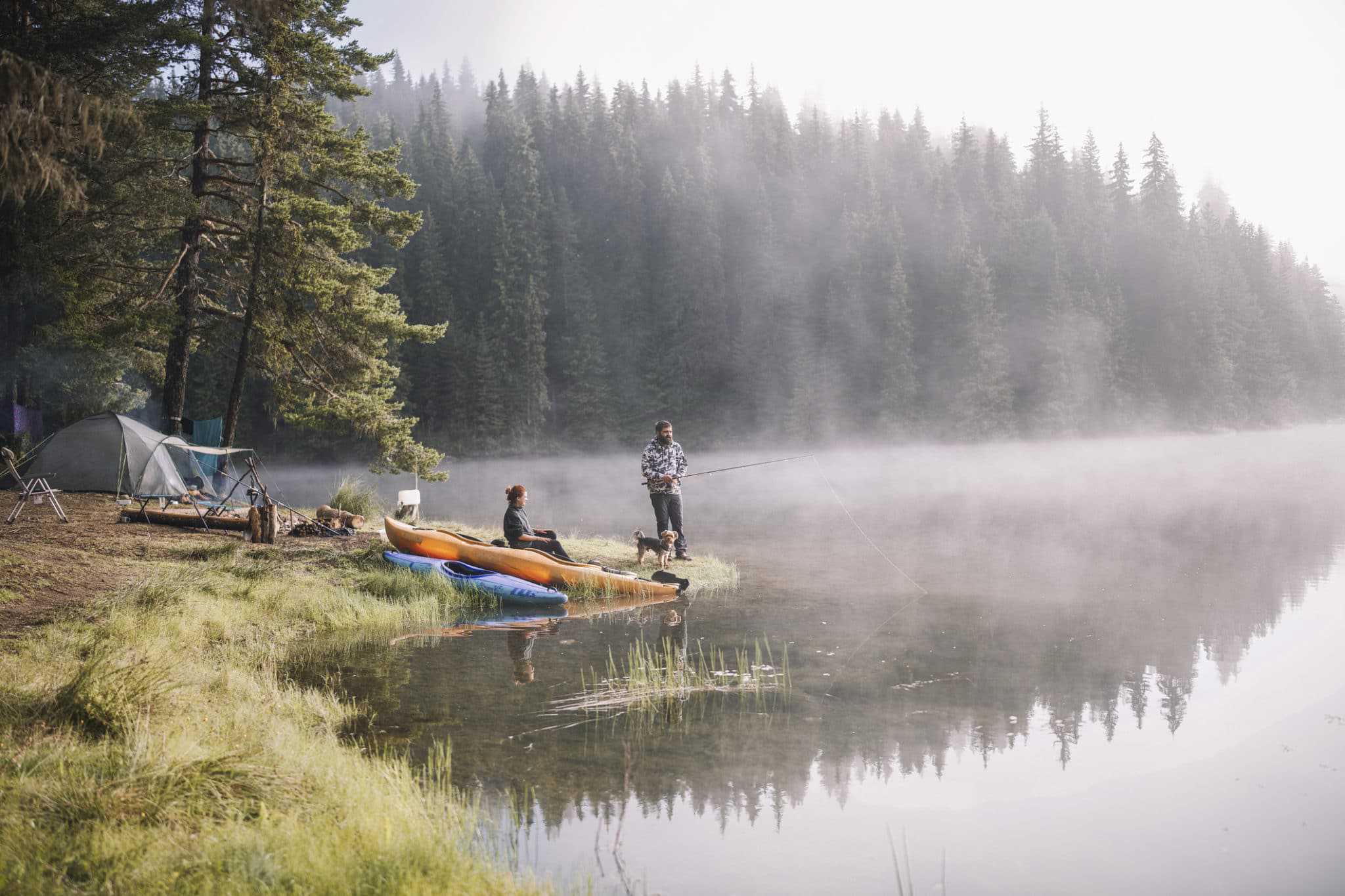 A couple enjoys a picturesque campsite in Tennessee, sitting on the shore of a lake with their kayaks nearby.