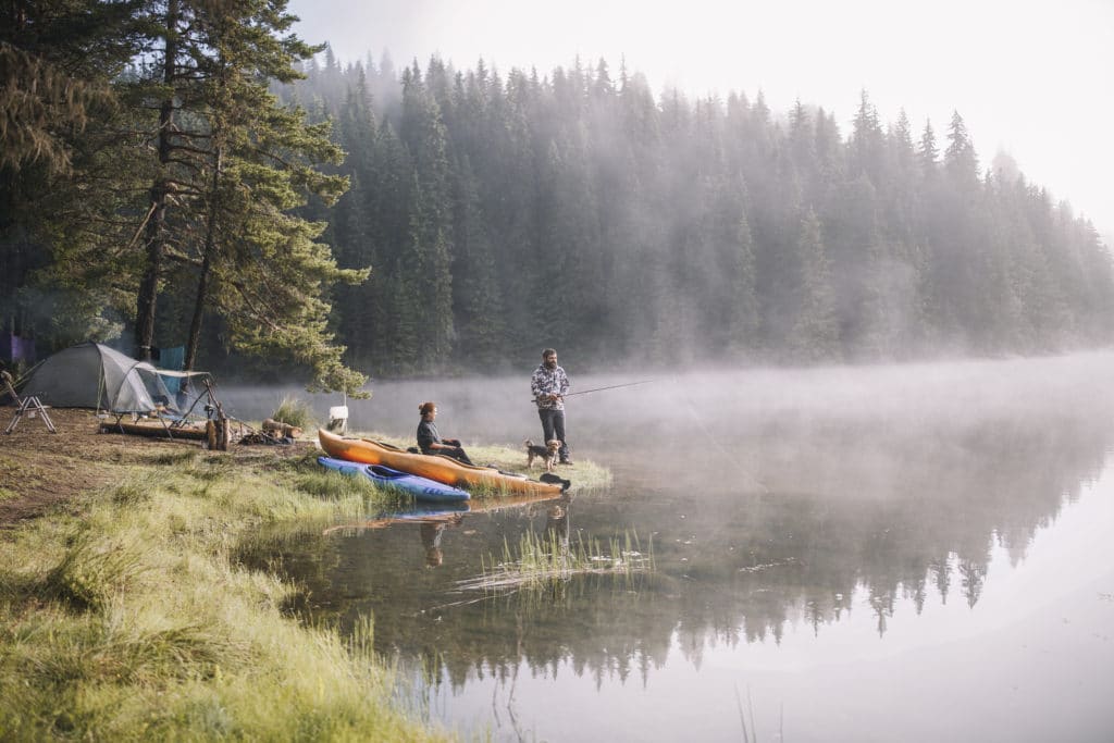 Two people sit on the shore of a lake with kayaks.