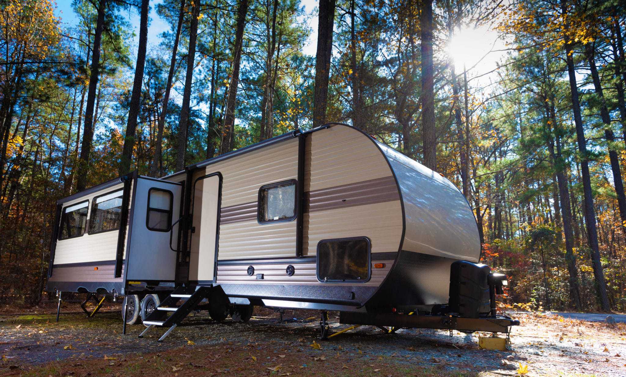 An upgraded travel trailer parked in a wooded area with an Electric Trailer Tongue Jack.