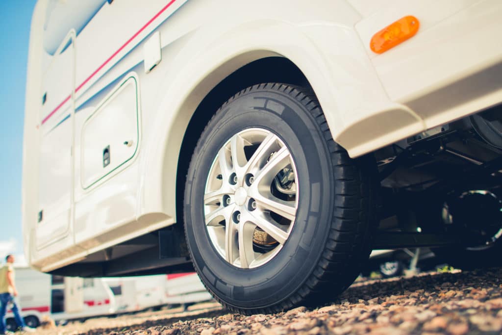 A white RV with a tire parked in a gravel lot, using a Run-Flat Device for RV Safety.