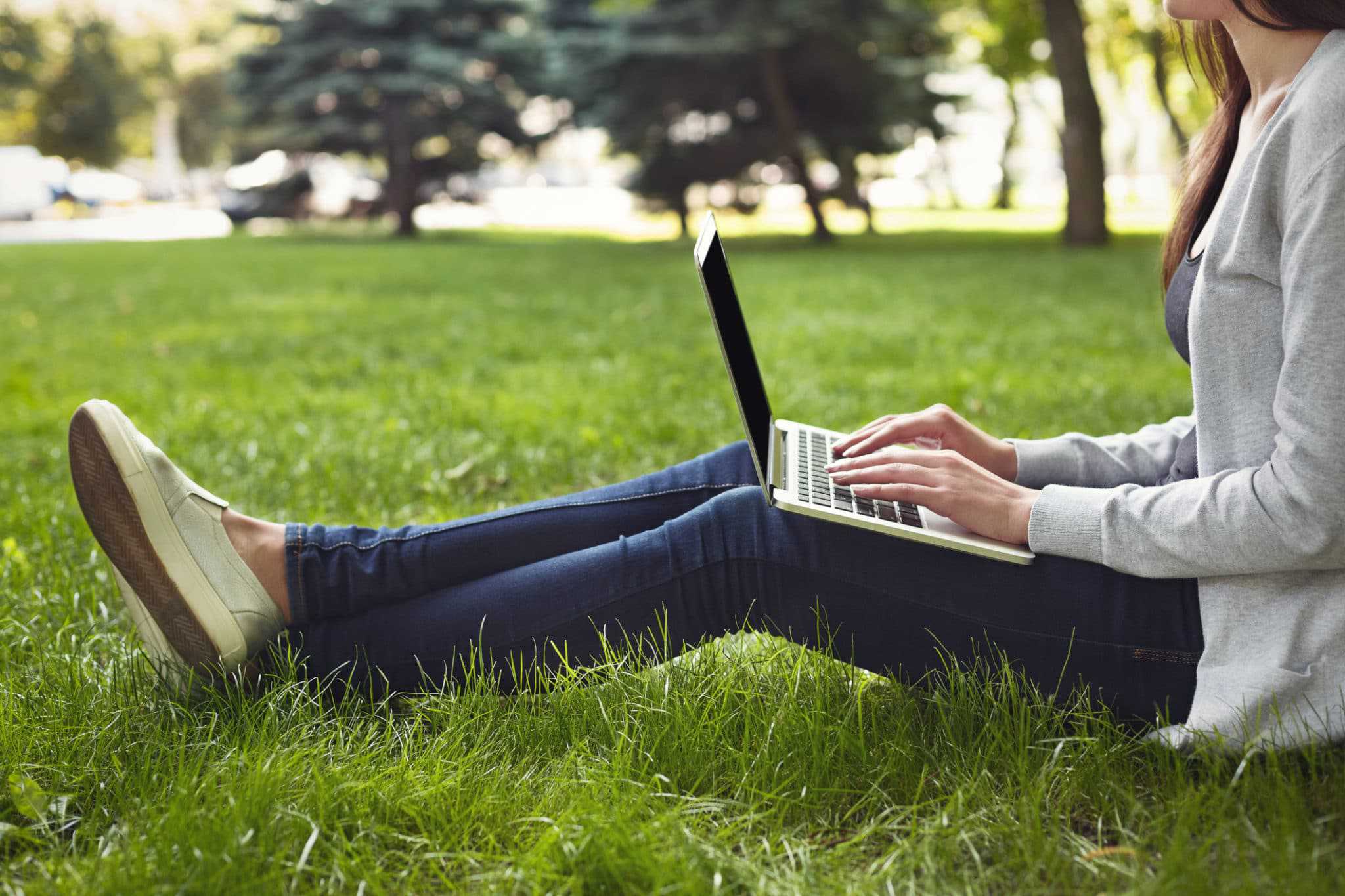 A young woman sitting on the grass in an outdoor space with a laptop, enjoying the benefits of GoZone WiFi.