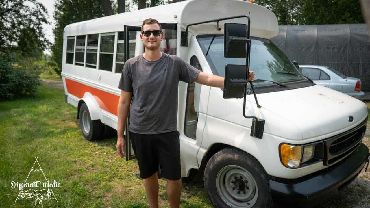 A man standing next to a white and orange school bus, transformed into a "condo on wheels" for his vanlife adventure.