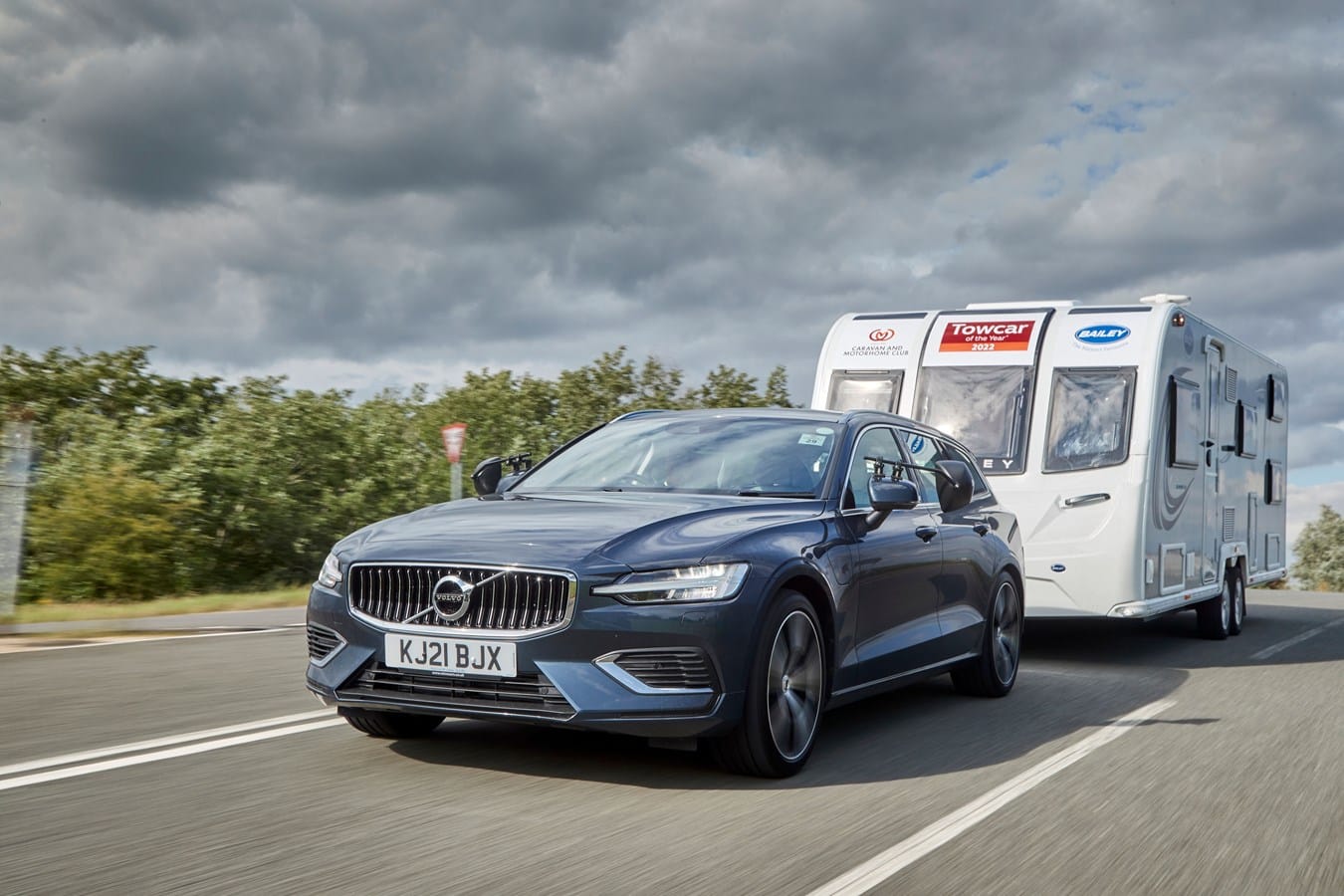 The Volvo V60, an electrified model, is driving down the road with a trailer behind it.