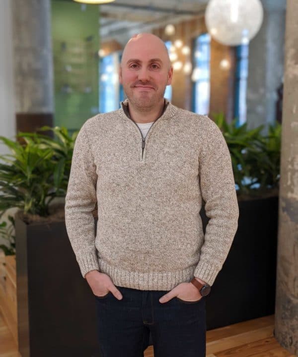 An MC in a sweater standing in an office, engaging in Fireside Chats.