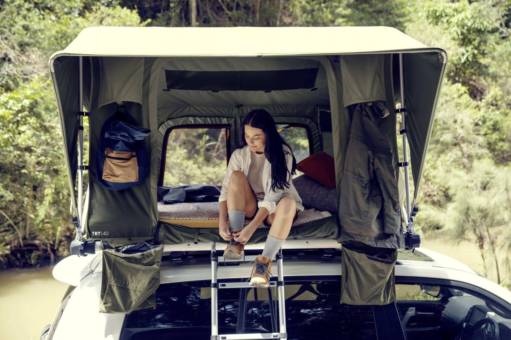 A woman sits on the roof of a car with a rooftop tent.