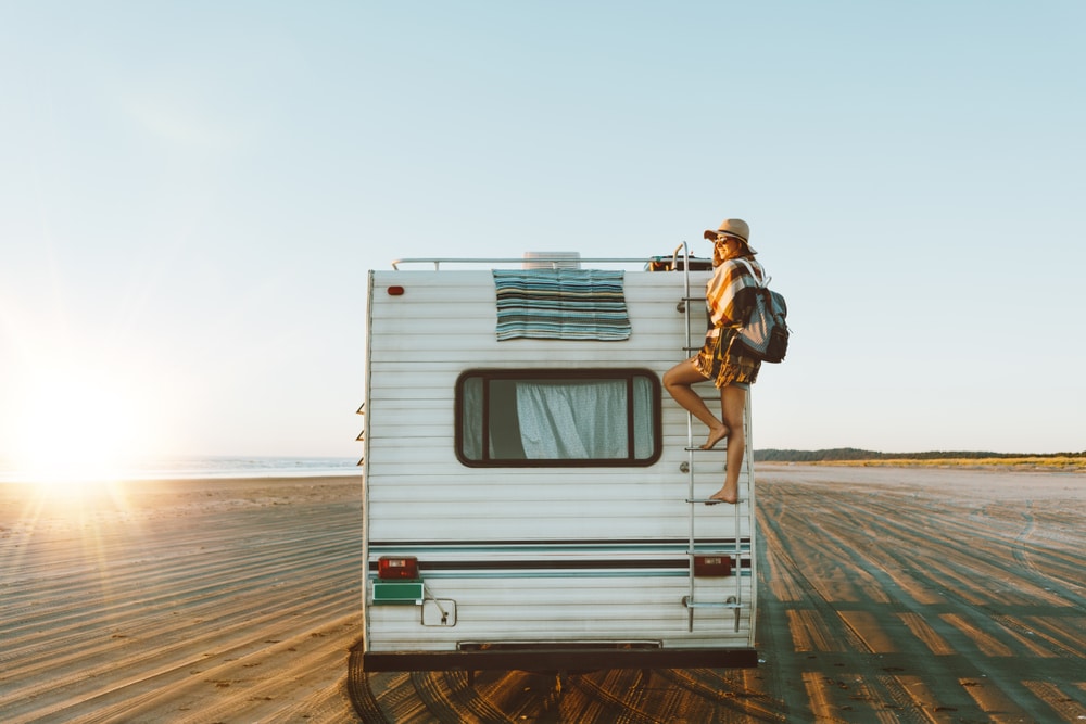 A man standing on top of an RV on the beach, representing RVezy, one of Canada’s Top Growing Companies.