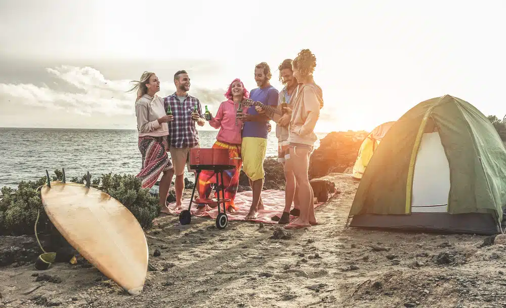 A group of friends standing near a tent on the beach.