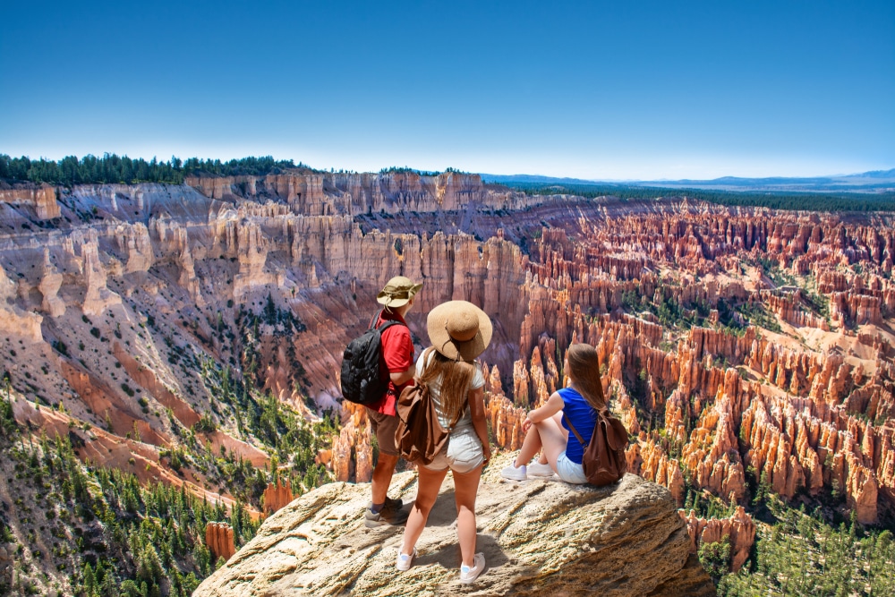 Three Americans standing on top of a cliff overlooking Bryce Canyon during their fall travel plans.