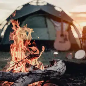 A campfire in front of a tent and guitar.