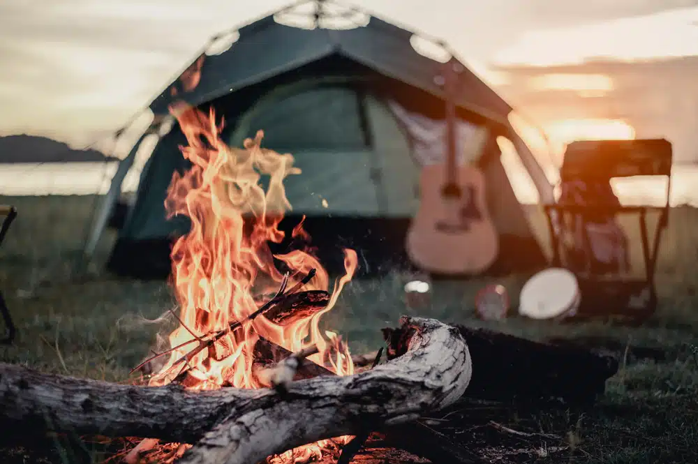 A campfire in front of a tent and guitar.