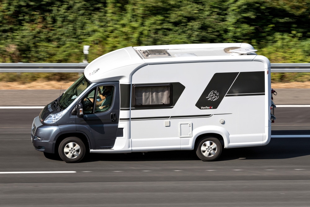 A Knaus Tabbert motorhome driving down a highway with trees in the background, showcasing its positive balance.