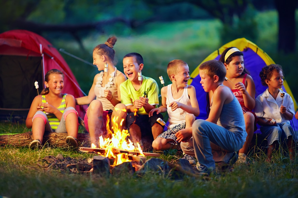 A group of kids sitting around a campfire at a campground.