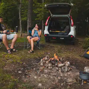 Two people sitting around a campfire in the woods.