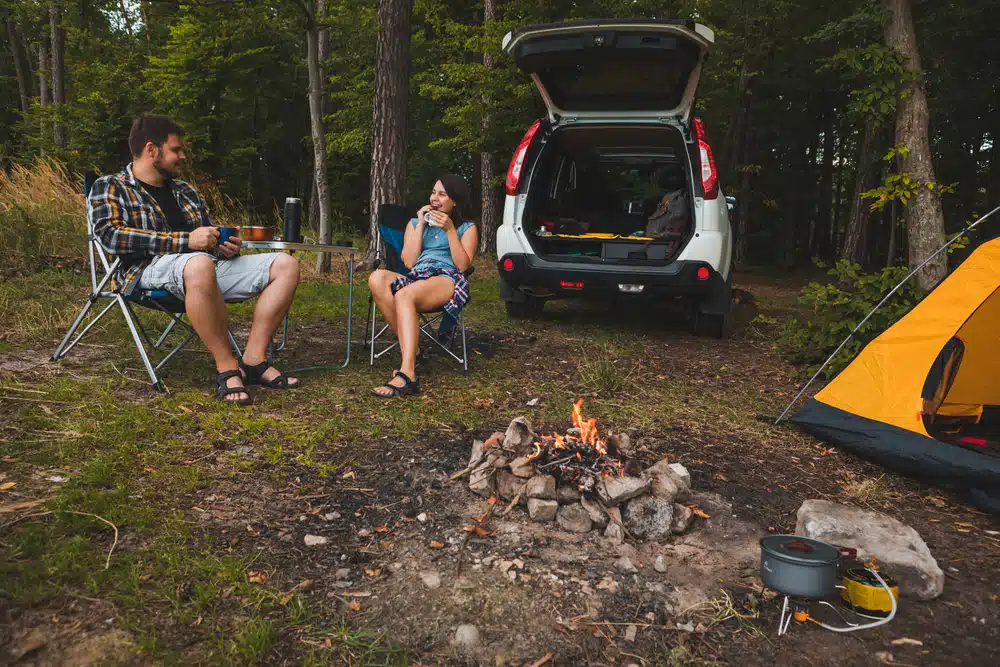 Two people sitting around a campfire in the woods.