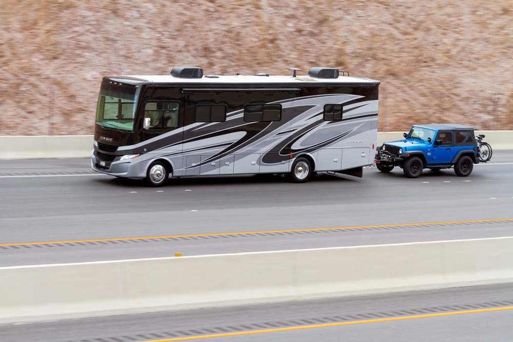 An American Coach RV with a jeep behind it, enjoying fall vistas and passing by stunning waterfalls along the way.