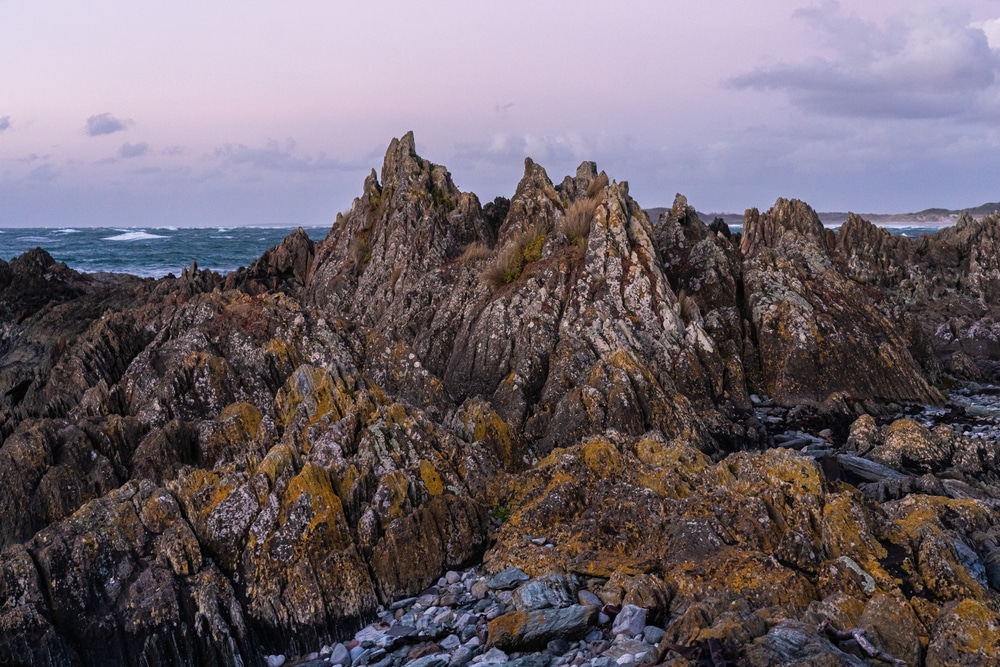 Rocky cliffs on a beach at dusk, ideal for camping.