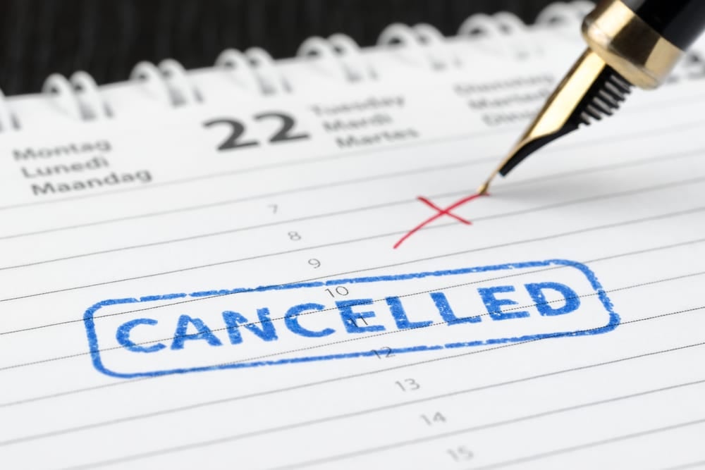 A pen is writing the word cancelled on a calendar.