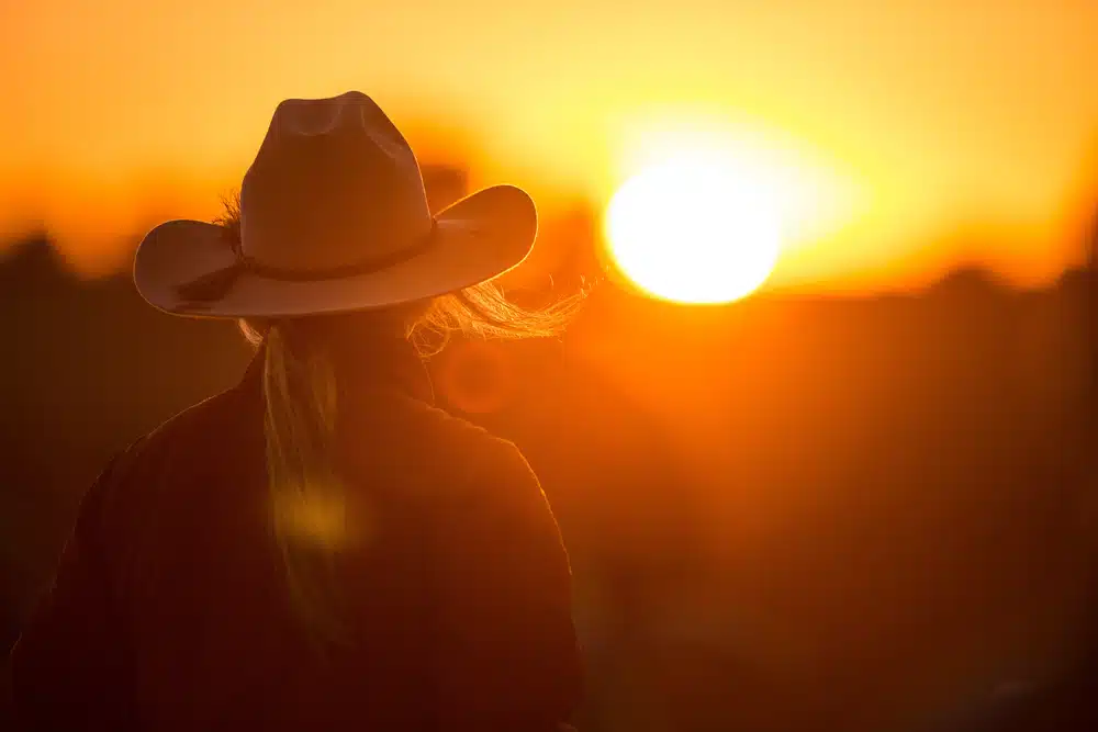 A woman wearing a cowboy hat at sunset.