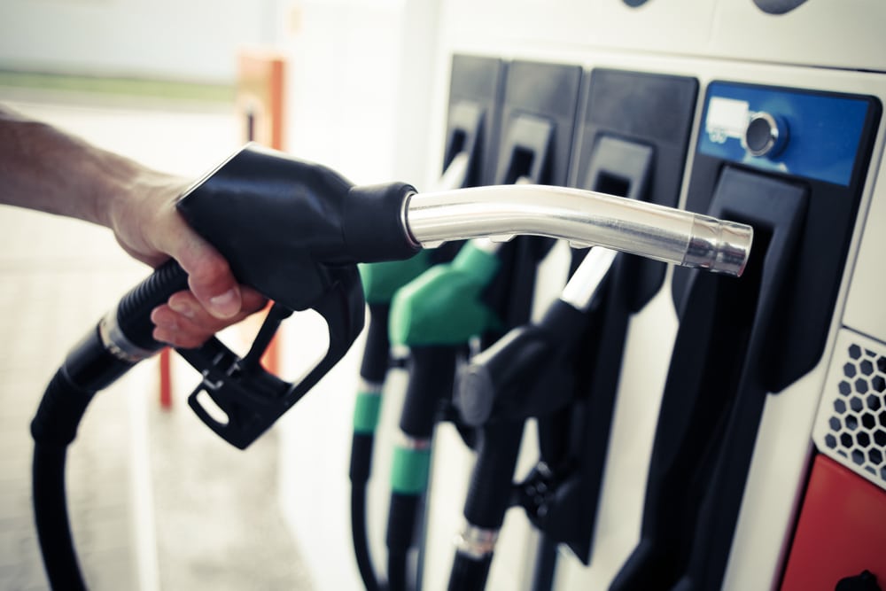 A person is filling up a gas tank at a gas station while observing the stability of oil prices.