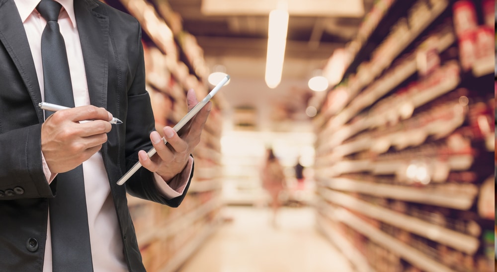 A man in a suit is holding a tablet in a grocery store, demonstrating consumer confidence.
