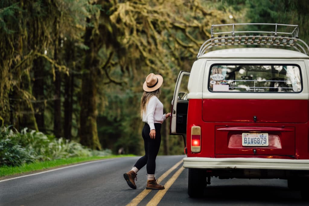 A woman standing next to a vw camper van on the road, embracing the spirit of Roamly.