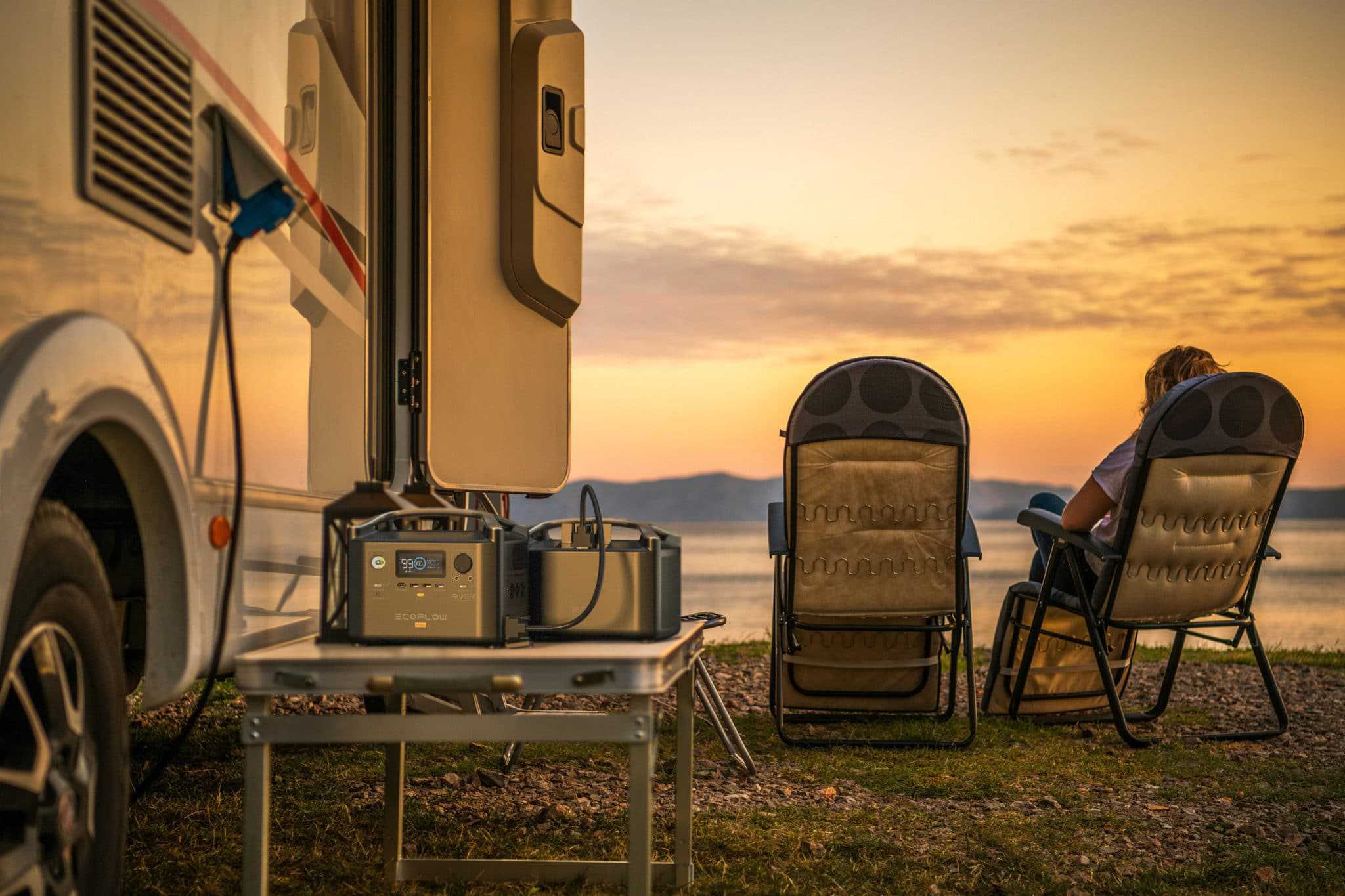 Two people sitting in chairs in front of an RV at sunset, enjoying the outdoors with sustainable energy solutions from EcoFlow.