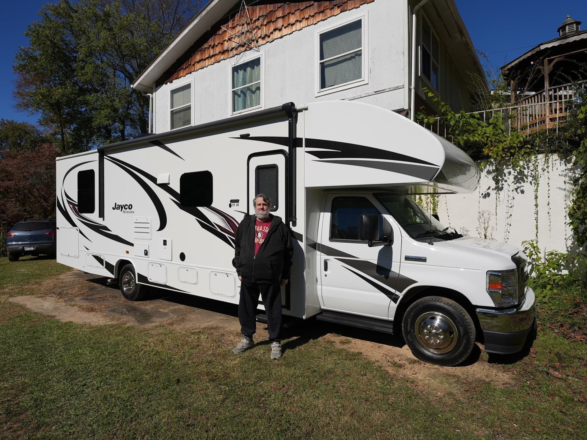 A man standing in front of his Jayco Redhawk Class C Motorhome, showcasing the Home of the Free Promotion offered by an RV Retailer.