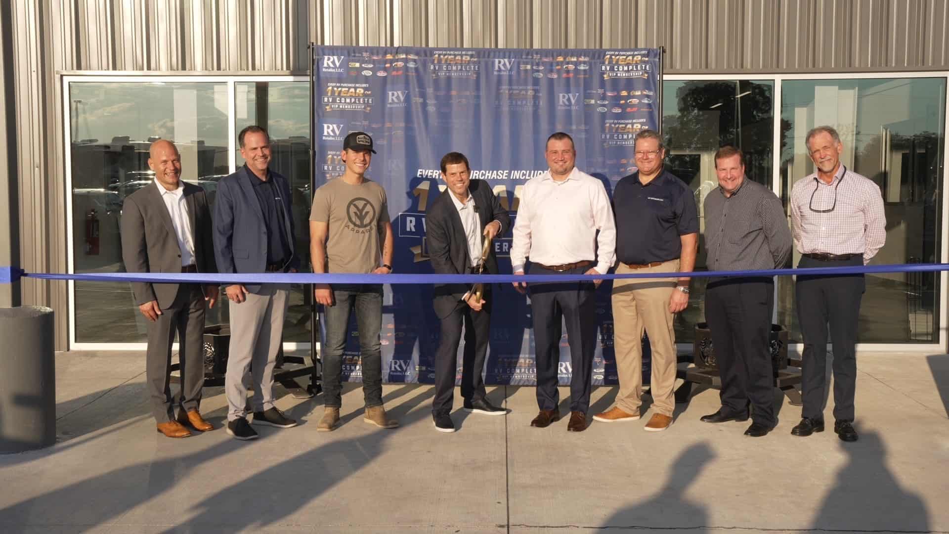 A group of RV Retailer employees standing proudly in front of a blue ribbon at one of their Texas stores.