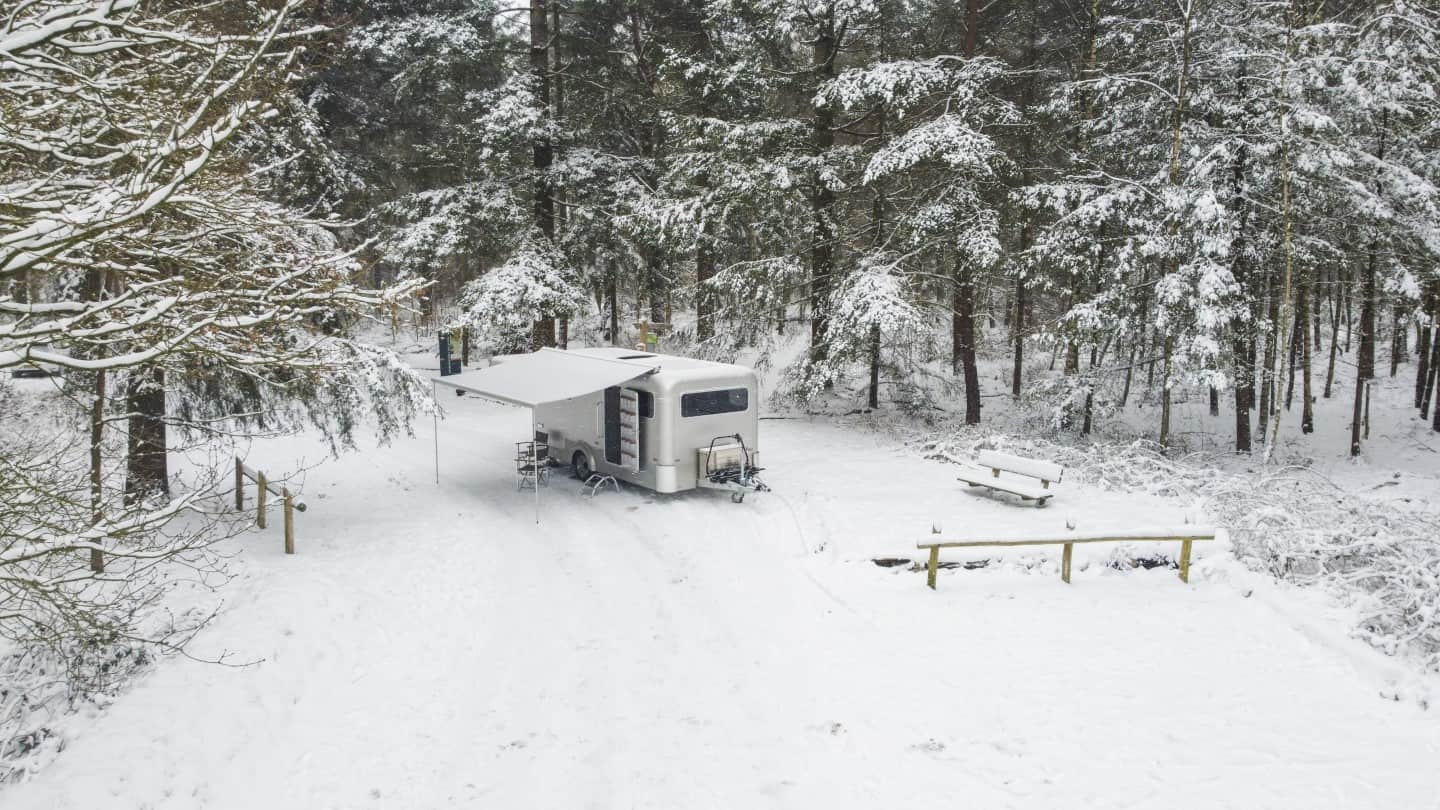 A Winter Glamping Retreat, featuring an Aluminum Caravan parked in a snow covered forest, expertly constructed by a Dutch Builder.