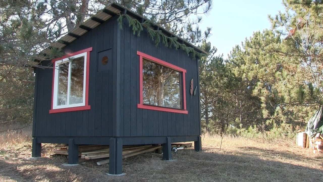 An affordable off-grid cabin nestled in the woods, featuring a charming red roof.