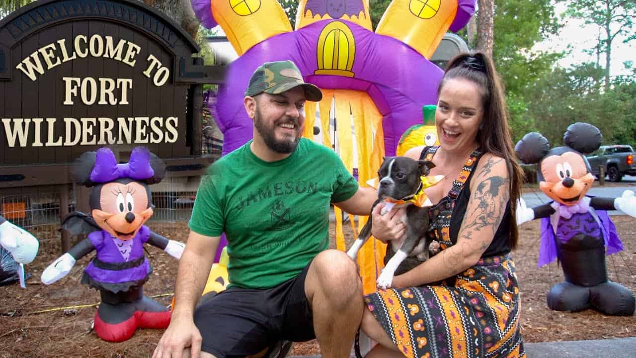 A man and woman pose with a dog in front of a welcome to Fort Wilderness sign at Disney's campgrounds.