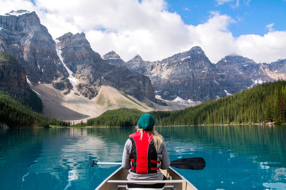 A woman is paddling a canoe on a lake in Banff National Park, showcasing the beauty of Canada's tourism.