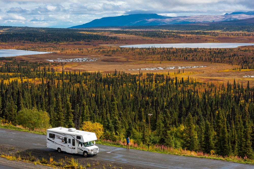 An RV parked on a road, surrounded by majestic mountains in the background.