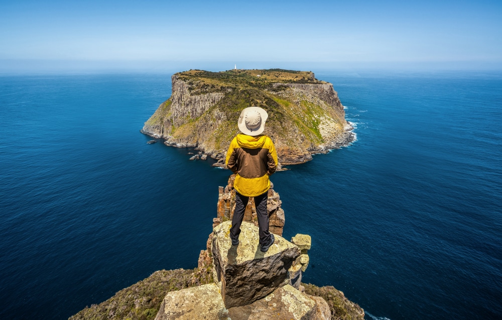 An Australian woman is standing on top of a rock overlooking the ocean.