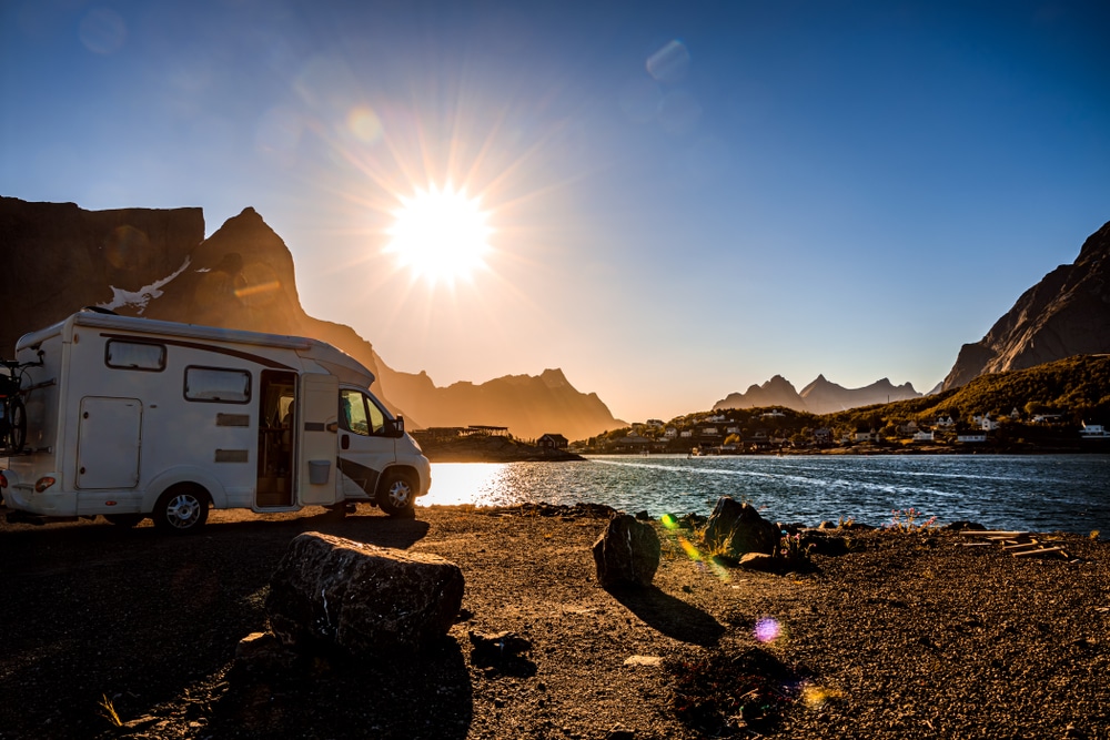 A scenic landscape featuring an RV parked in front of a serene lake, complemented by the majestic backdrop of mountains.