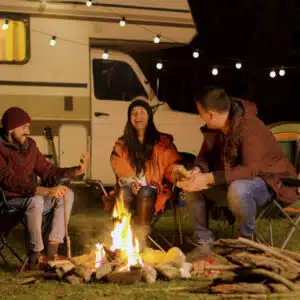Three Australians sitting around a campfire in front of an RV in the bush.