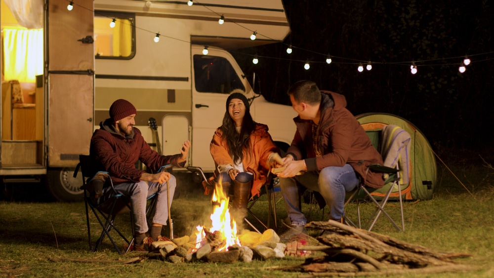 Three Australians sitting around a campfire in front of an RV in the bush.