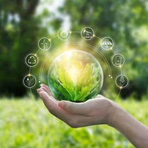 A woman's hand holding a glass ball with green leaves on it, representing sustainability and recycled material.