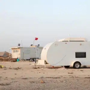A white camper parked on the sandy beach in Qatar, providing a unique winter camping experience close to nature.