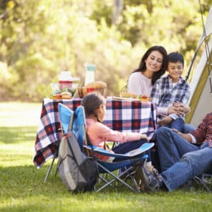 A Latinx family enjoys a picnic at a KOA campground, surrounded by lush greenery and their cozy tent. With this growing opportunity for outdoor exploration, they create lasting memories in nature.
