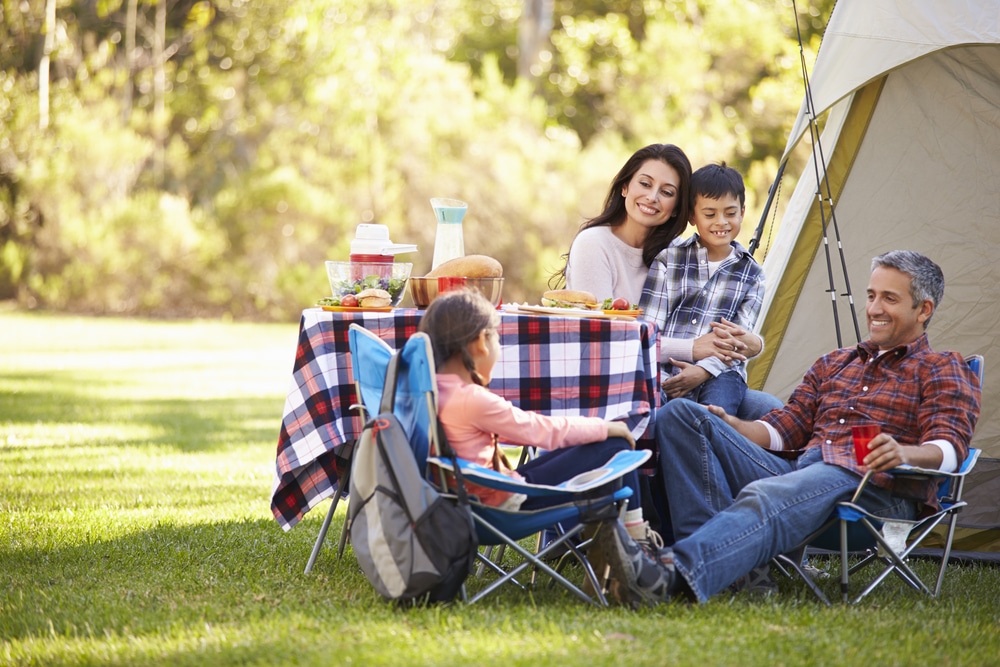 A Latinx family enjoys a picnic at a KOA campground, surrounded by lush greenery and their cozy tent. With this growing opportunity for outdoor exploration, they create lasting memories in nature.