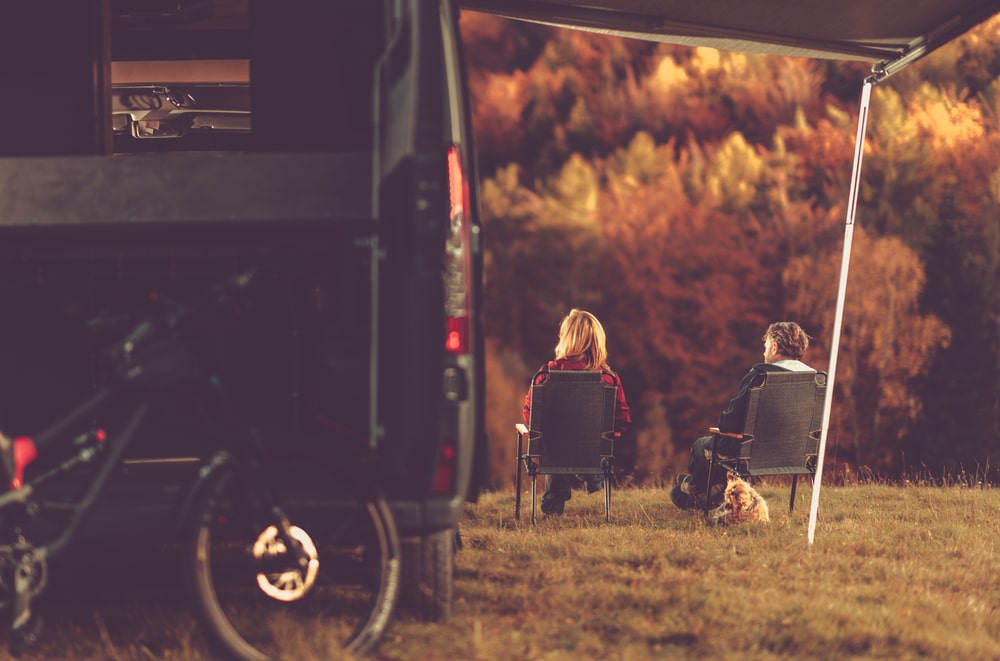 Two people sitting in front of a camper, enjoying the outdoors as part of REI's #OptOutside Campaign.