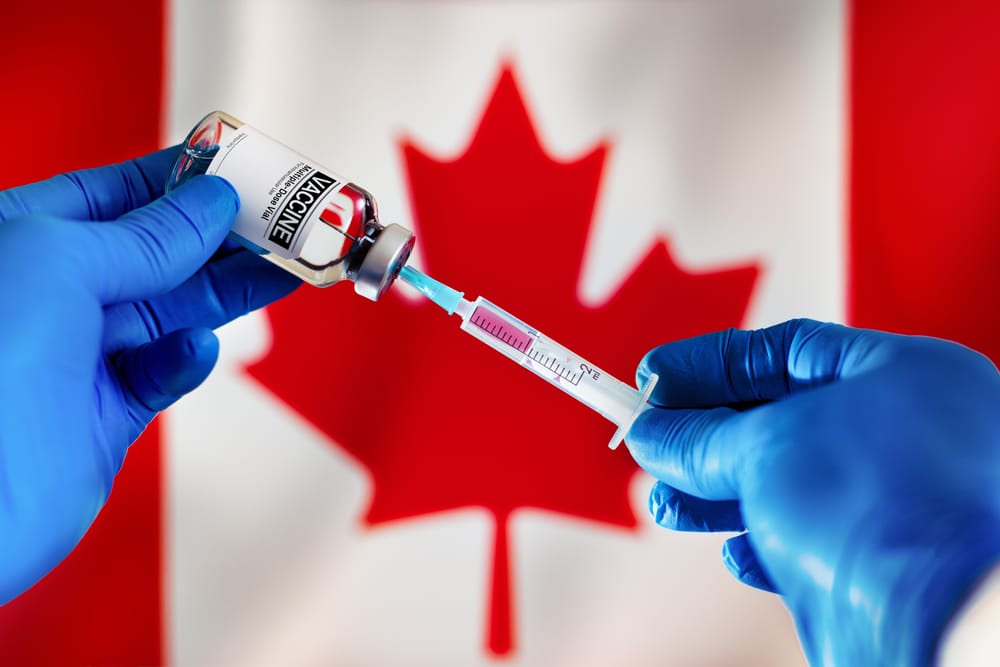 A person is holding a syringe in front of a Canadian flag to symbolize the implementation of vaccination rules in the Canada travel and tourism sector.