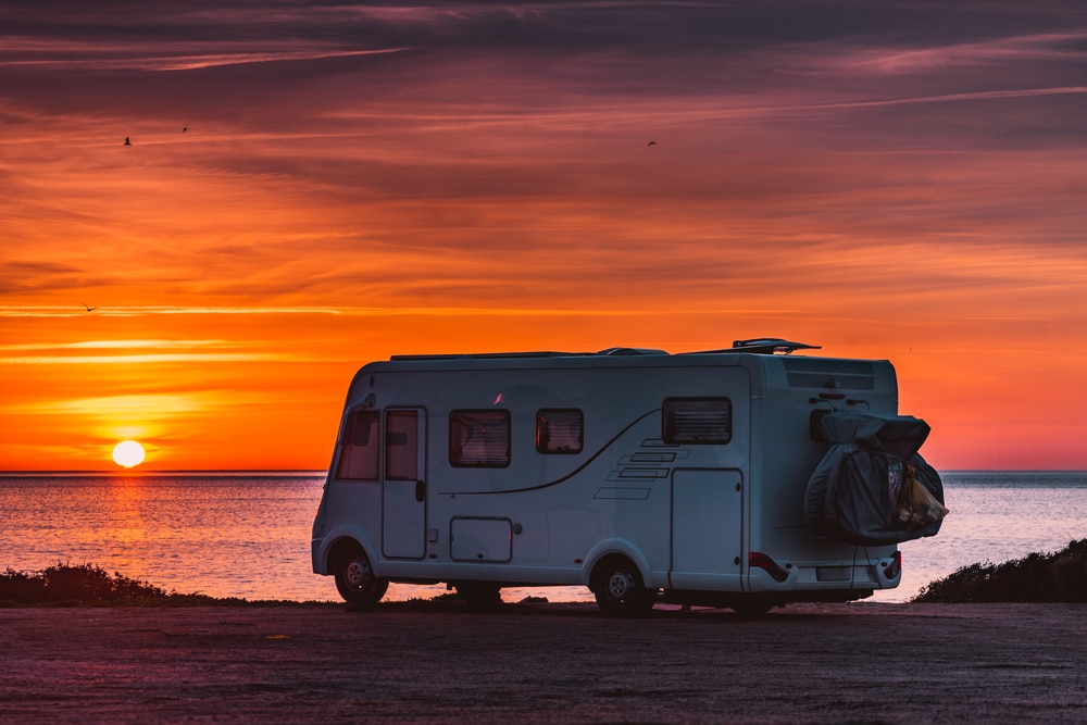 A white RV parked on the beach, creating a serene scene at sunset.