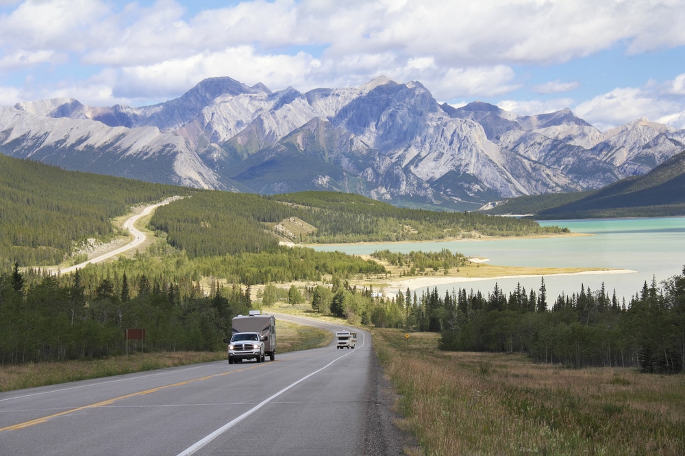 A truck, immersed in the serene beauty of a lake-enveloped background, embarks on a journey as it travels along the road.