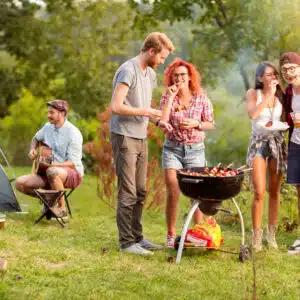 A group of friends enjoying a Camp Cooking barbecue at a campsite using the Box Braai/BBQ Grill from Front Runner Outfitters.