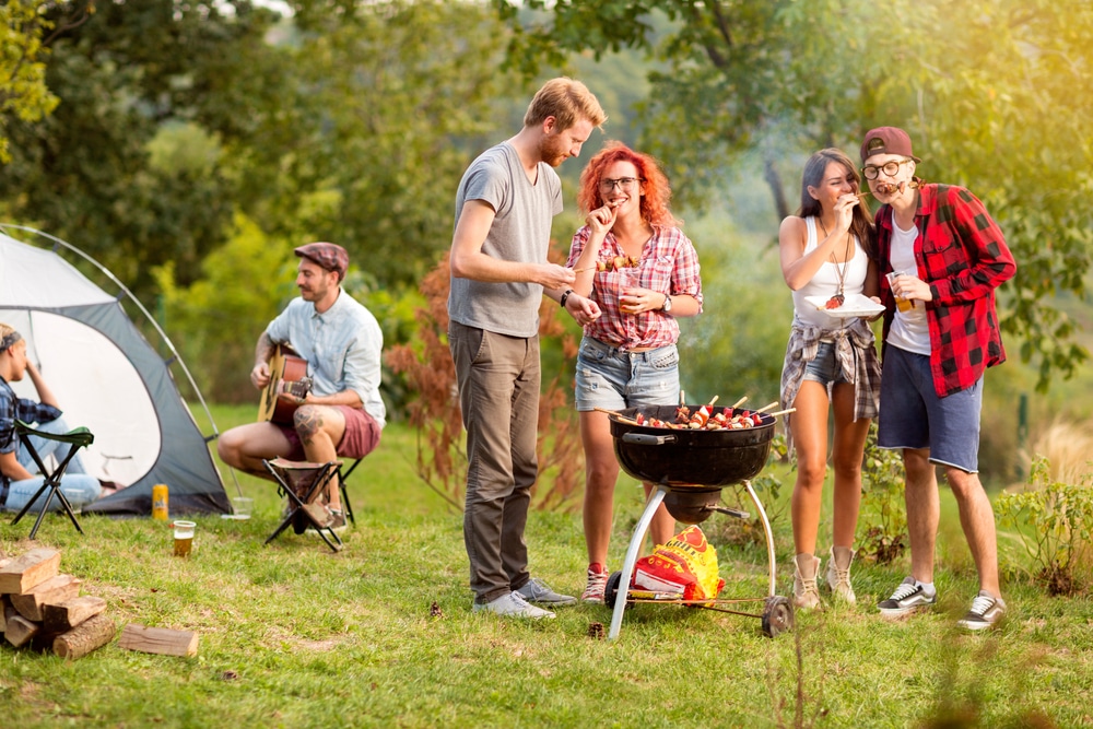 A group of friends enjoying a Camp Cooking barbecue at a campsite using the Box Braai/BBQ Grill from Front Runner Outfitters.