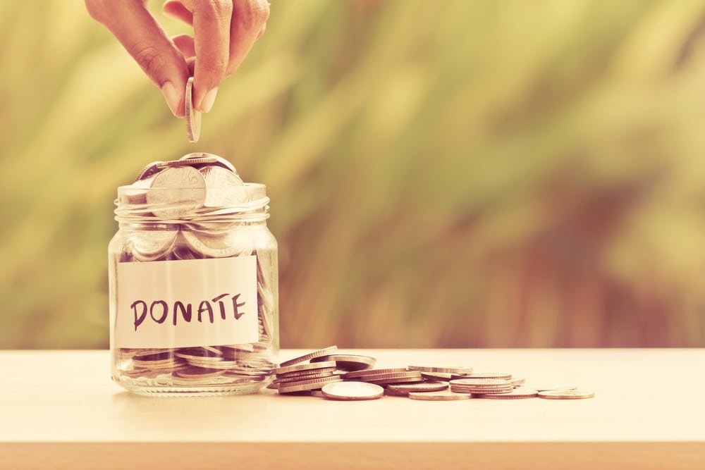 A person diligently placing coins into a jar labeled "donate" for the Fire Department Equipment Storage project.